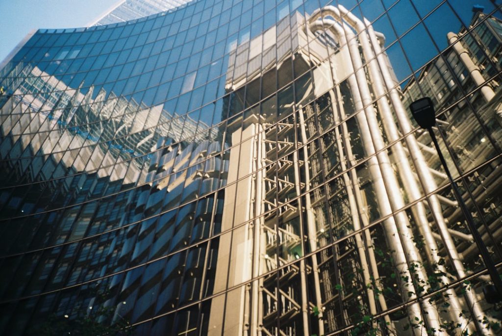 The futuristic architecture of the Lloyd’s building reflected in hundreds of windows of offices nearby on a bright, clear day in the City of London. Shot on film.